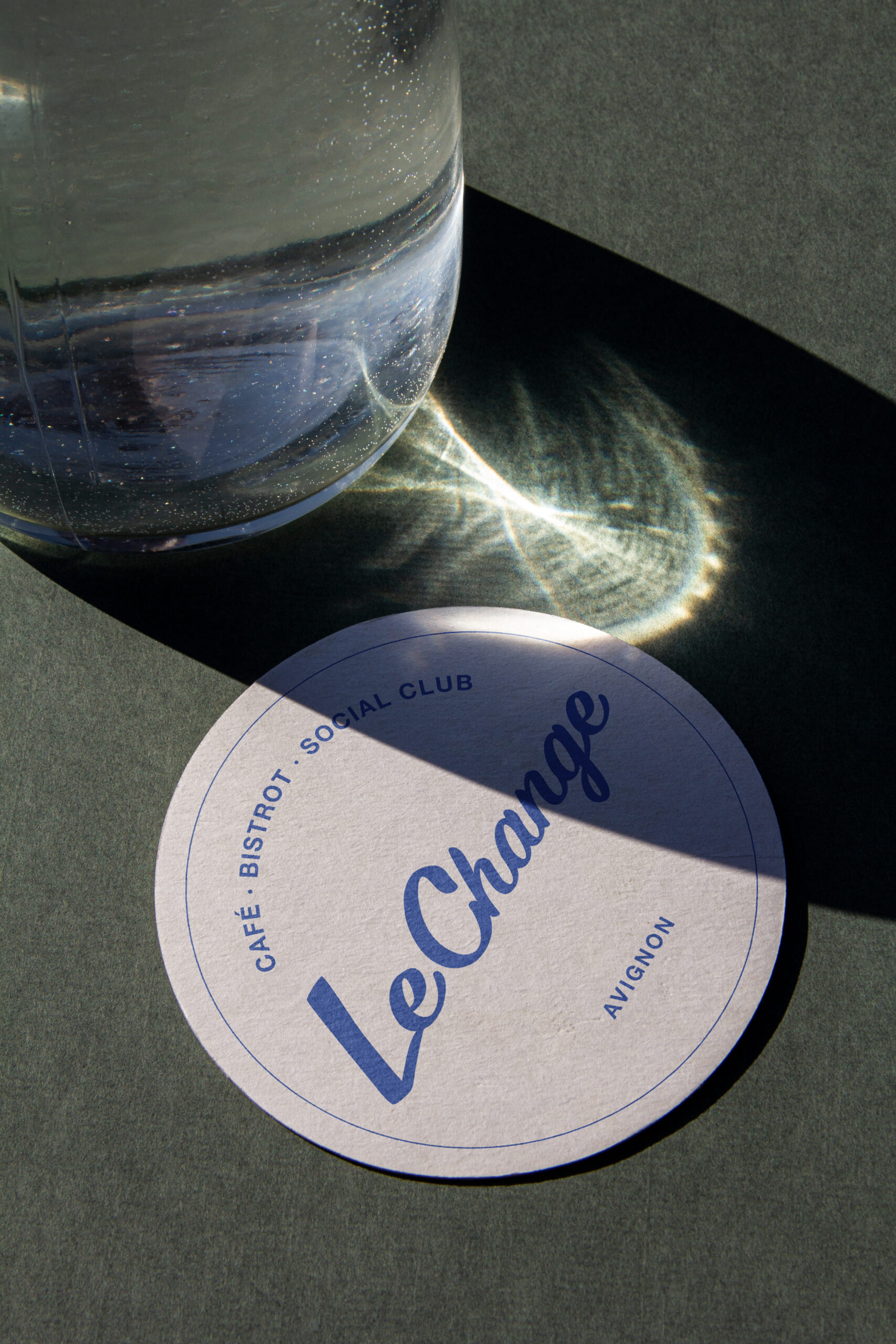 Dessous de verre clair Le Change sous un verre, avec le logo bleu.
