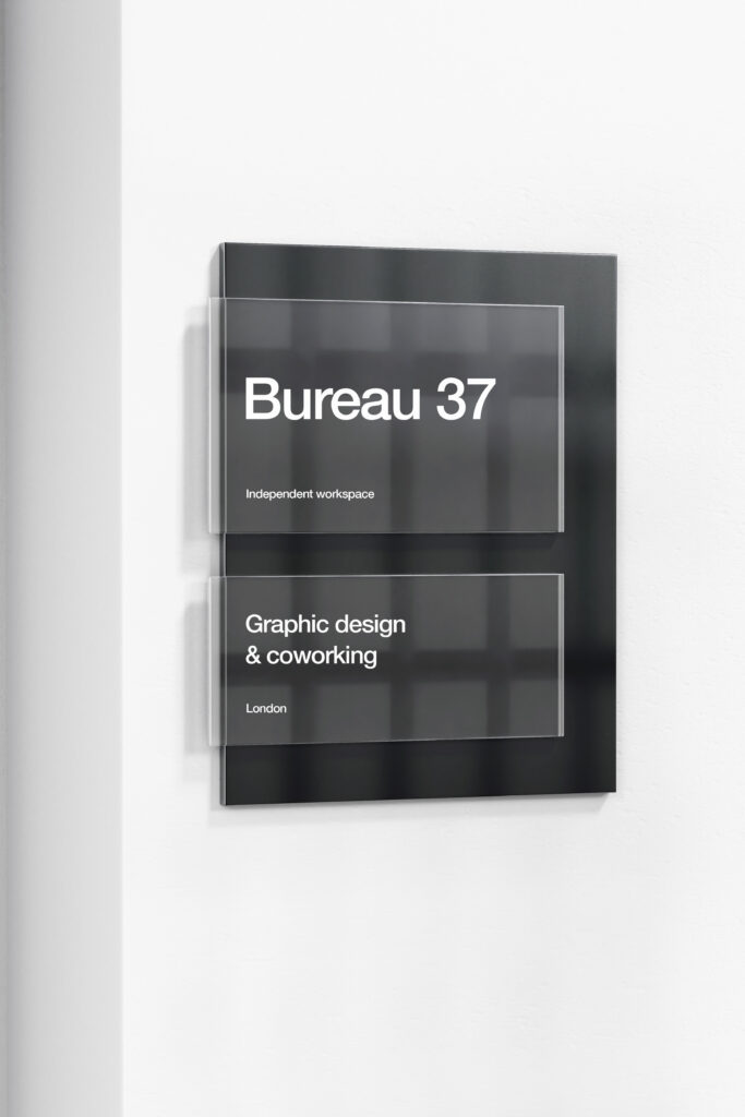Plaques murales noires Bureau 37, avec les inscriptions « Graphic design & coworking » et « London » en blanc.