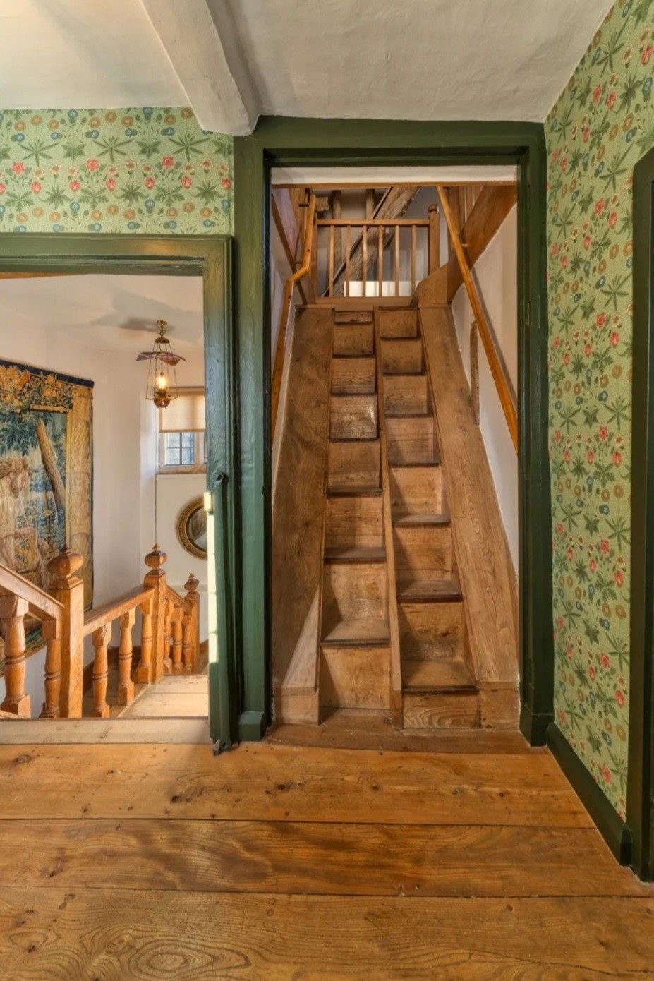 Escalier en bois et encadrements verts entourés d’un papier peint floral à Kelmscott Manor.