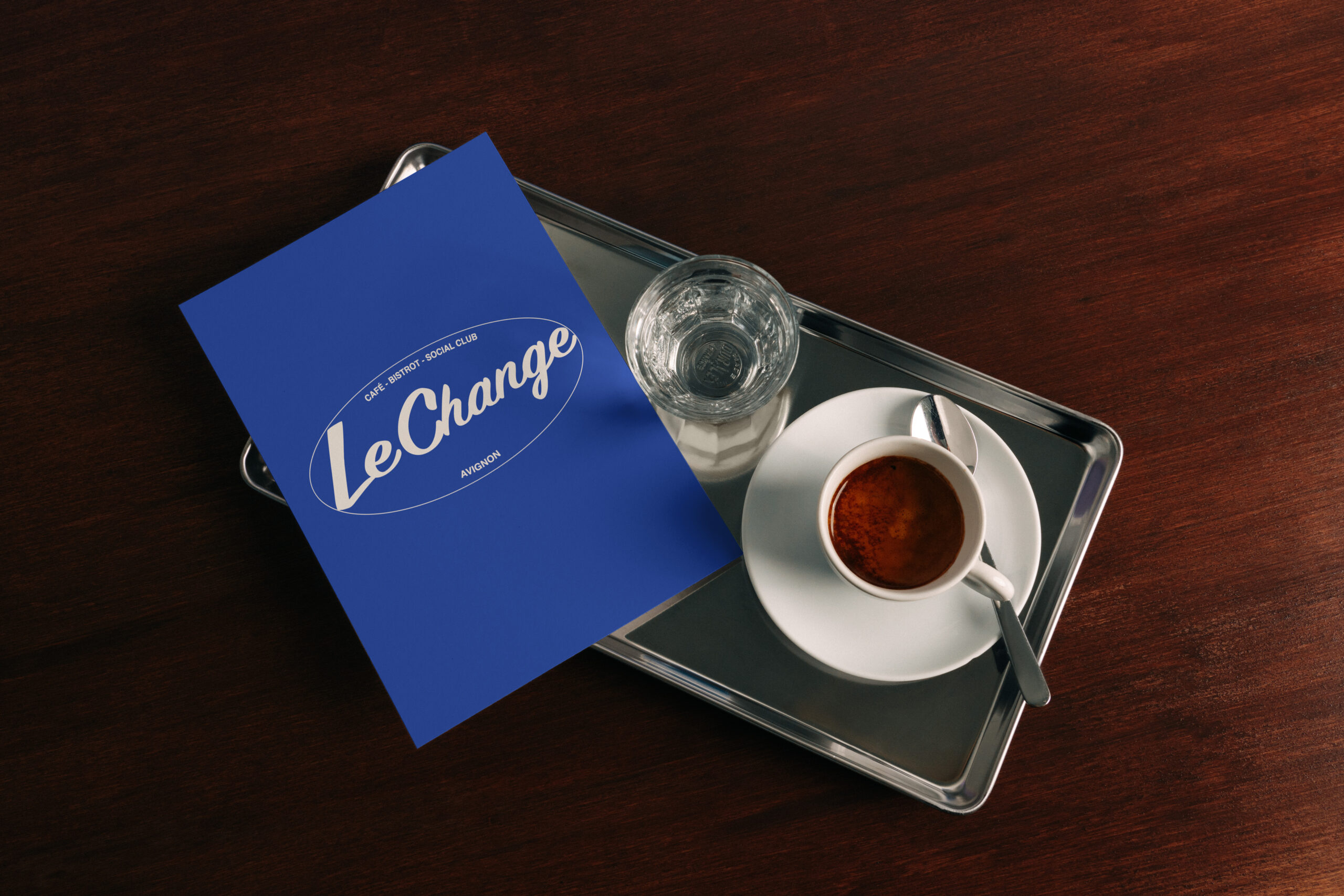 Carte bleue Le Change posée à côté d’un café et d’un verre sur un plateau.